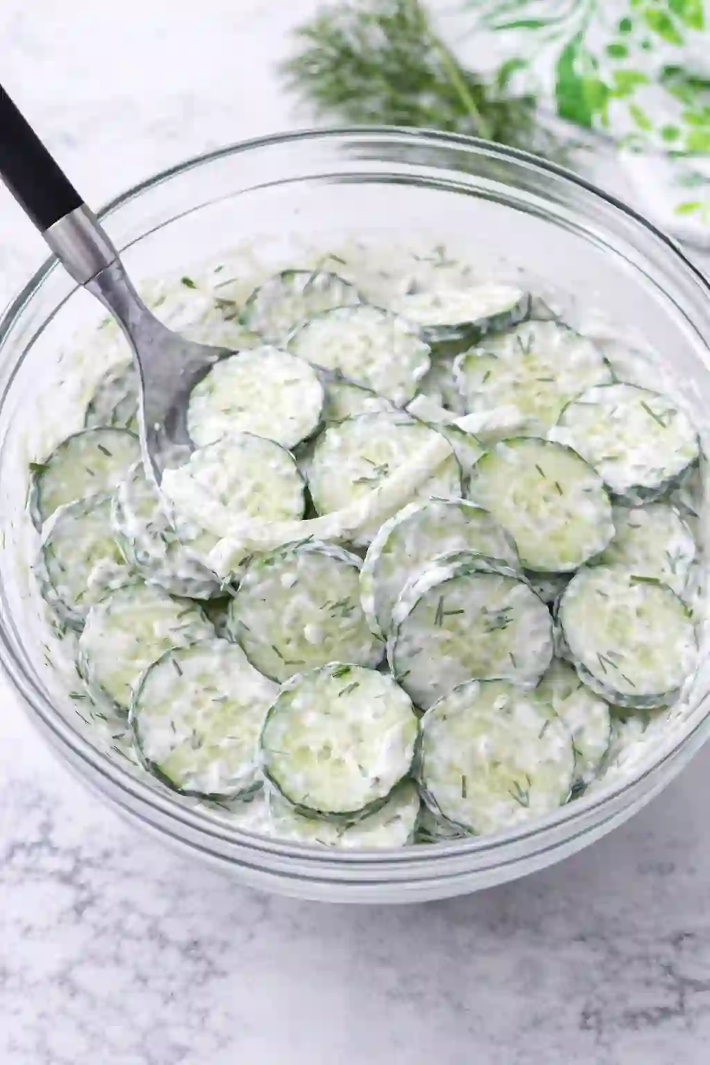 Mixing cucumbers with creamy dressing in a bowl for cucumber salad