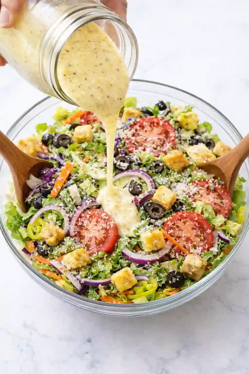 Creamy Italian dressing being poured over Olive Garden style salad in a glass bowl