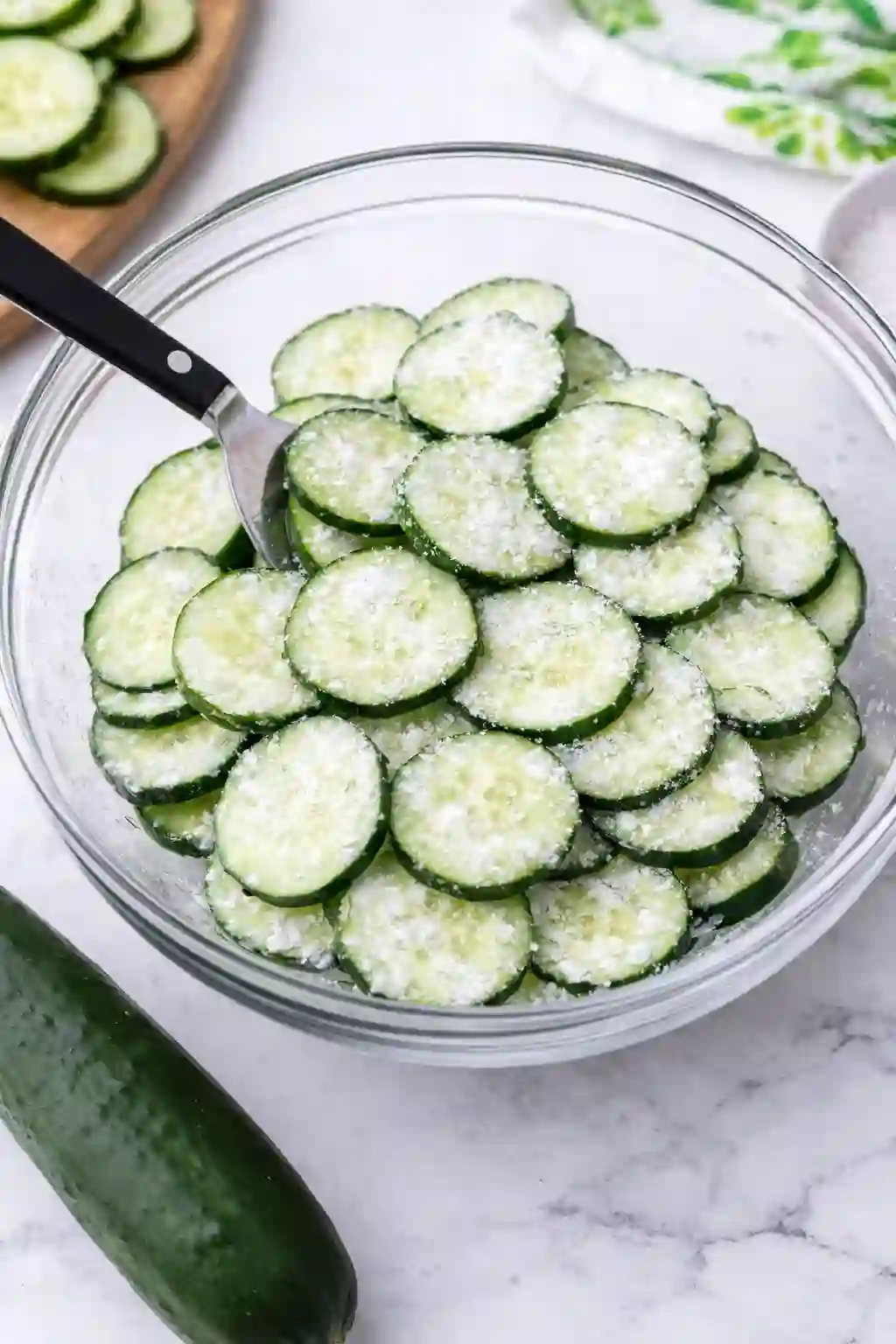 Salting sliced cucumbers in a bowl to remove excess water for creamy cucumber salad