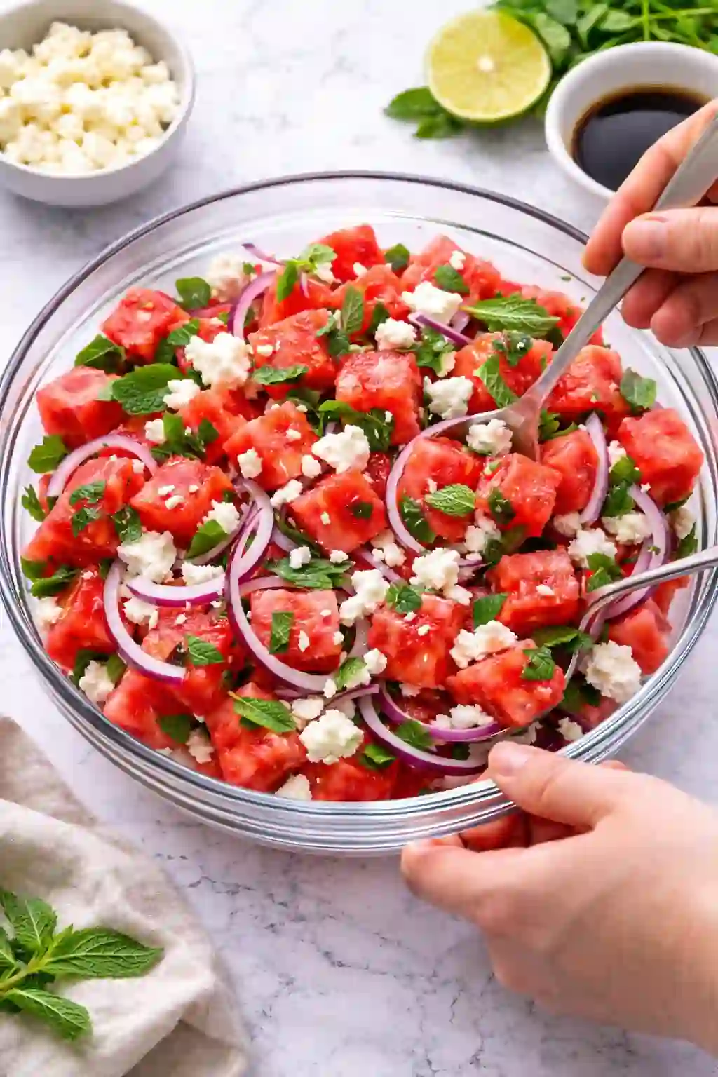 Tossing watermelon feta salad with mint and red onion in a bowl