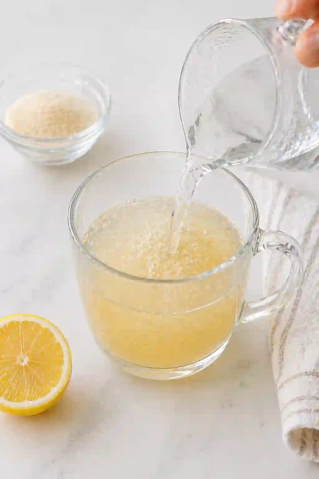 Pouring hot water into bloomed gelatin mixture in clear glass cup