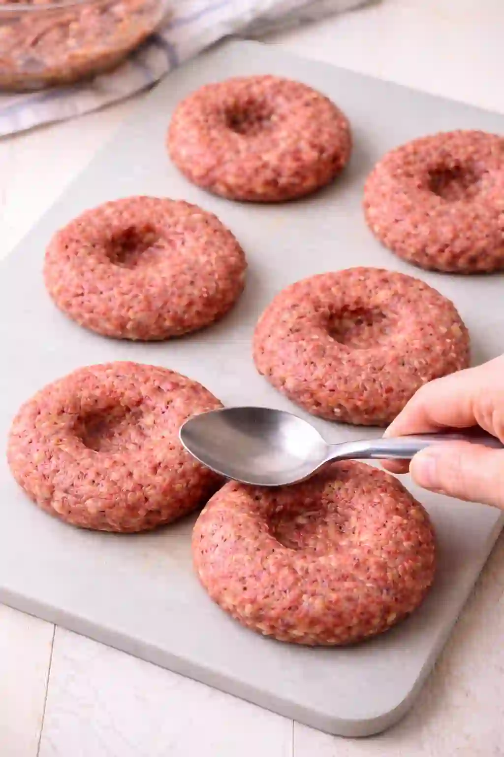 raw burger patties with center dent on cutting board ready for grilling