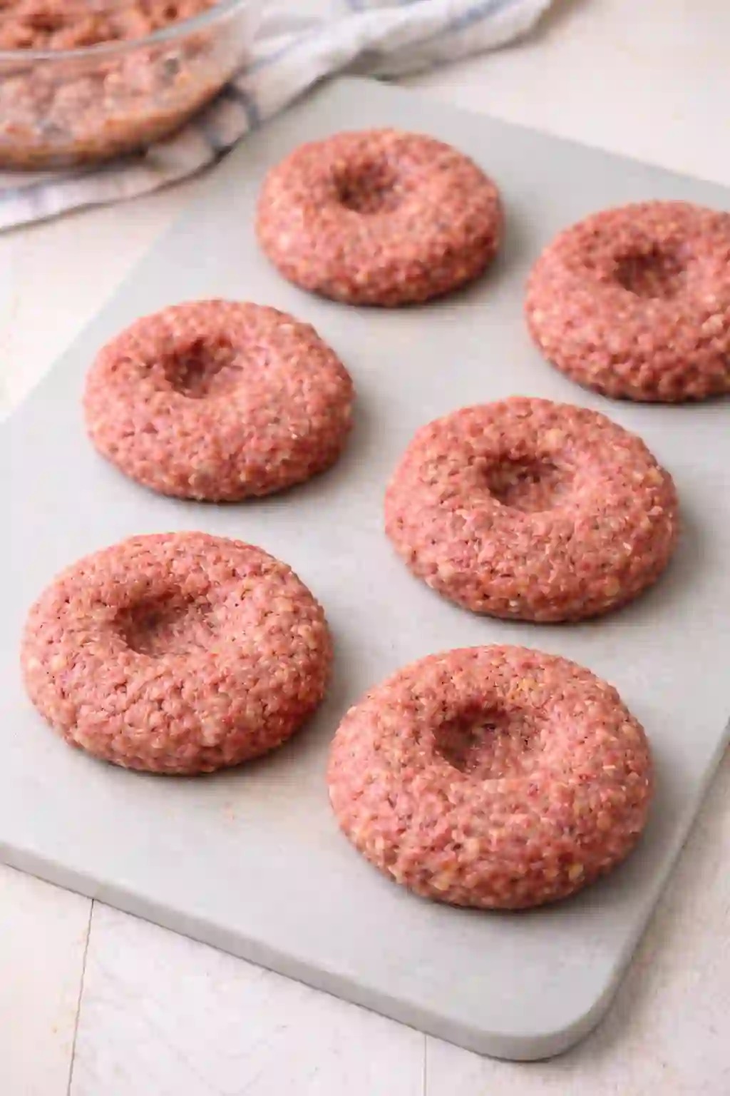 raw beef burger patties with thumbprint indentation on cutting board ready for grilling
