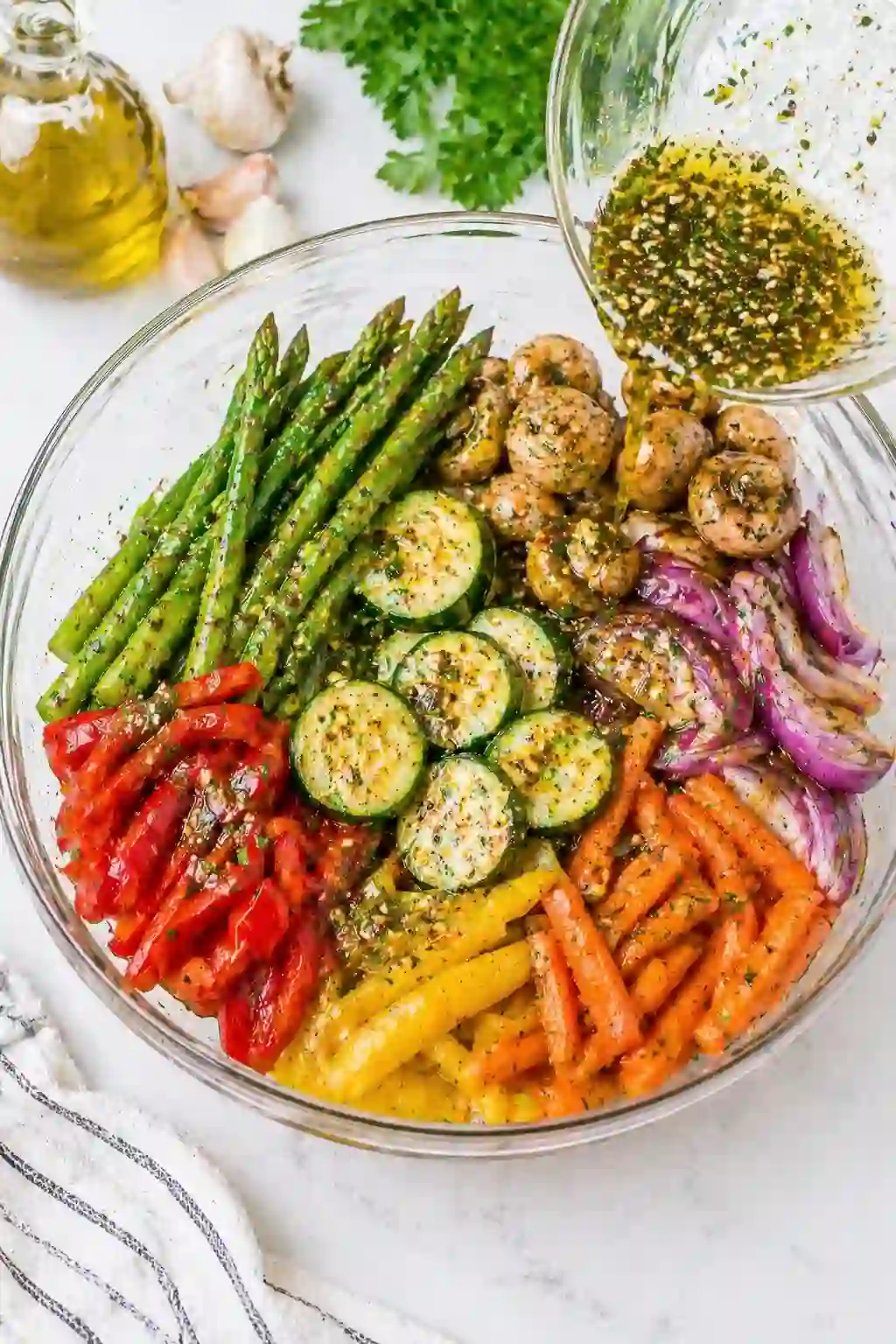 Coating vegetables with marinade for grilled vegetables recipe in a glass bowl with herbs and oil