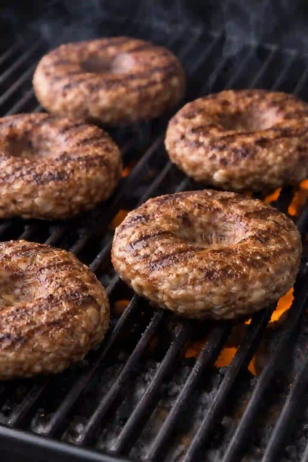 beef burger patties cooking on grill with grill marks and center dent visible