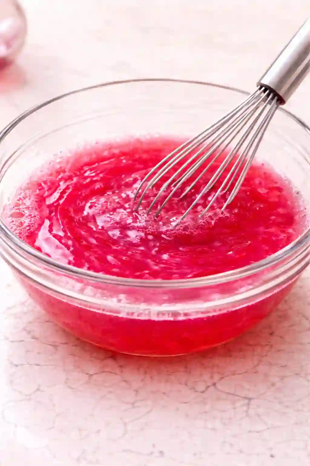 Whisking pink gelatin mixture in a glass bowl until smooth and fully dissolved