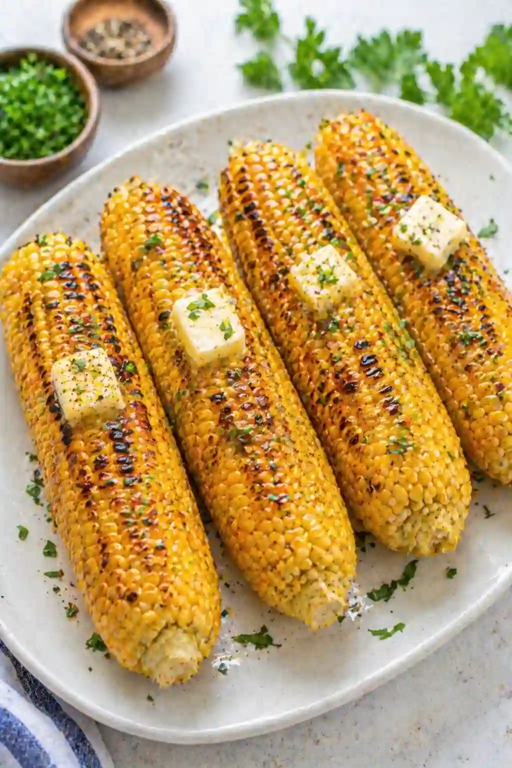 grilled corn on the cob on a plate with butter and herbs