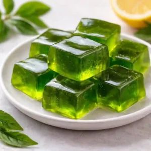 Green tea gelatin recipe for weight loss cubes served on a white plate with lemon and fresh tea leaves