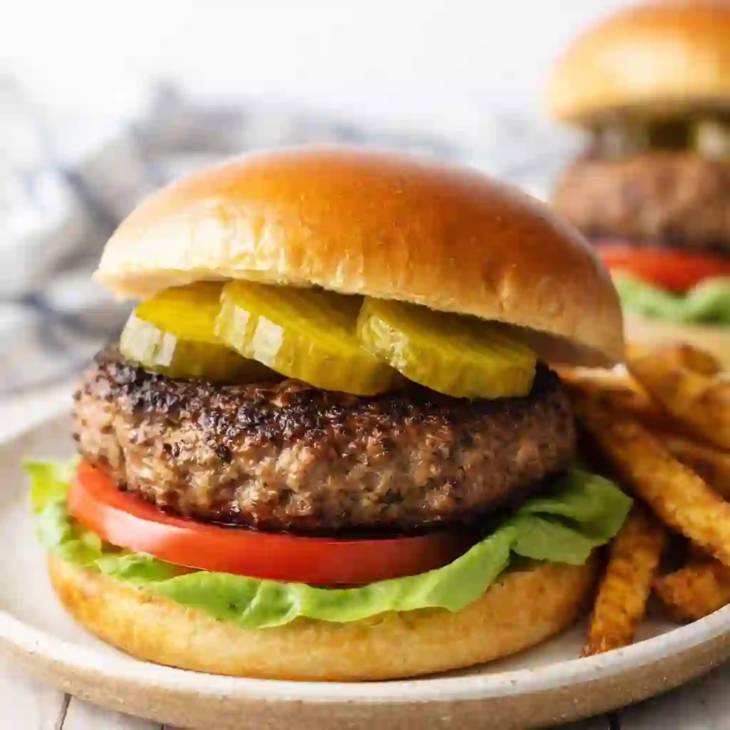 juicy grilled burger recipe with beef patty lettuce tomato and pickles on a plate