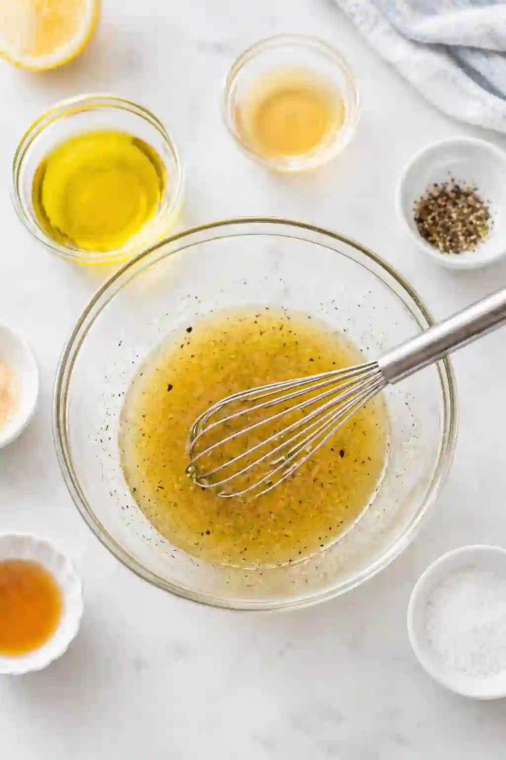Whisking vinegar coleslaw dressing in a glass bowl with oil and spices