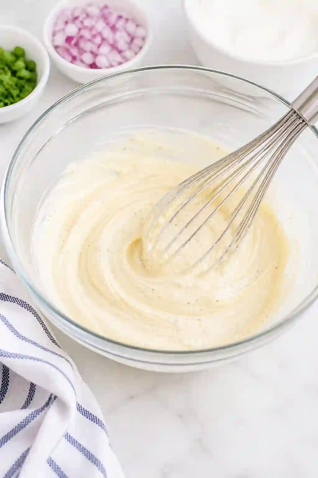 Mashed potatoes mixed into a creamy base in a bowl for BBQ potato salad